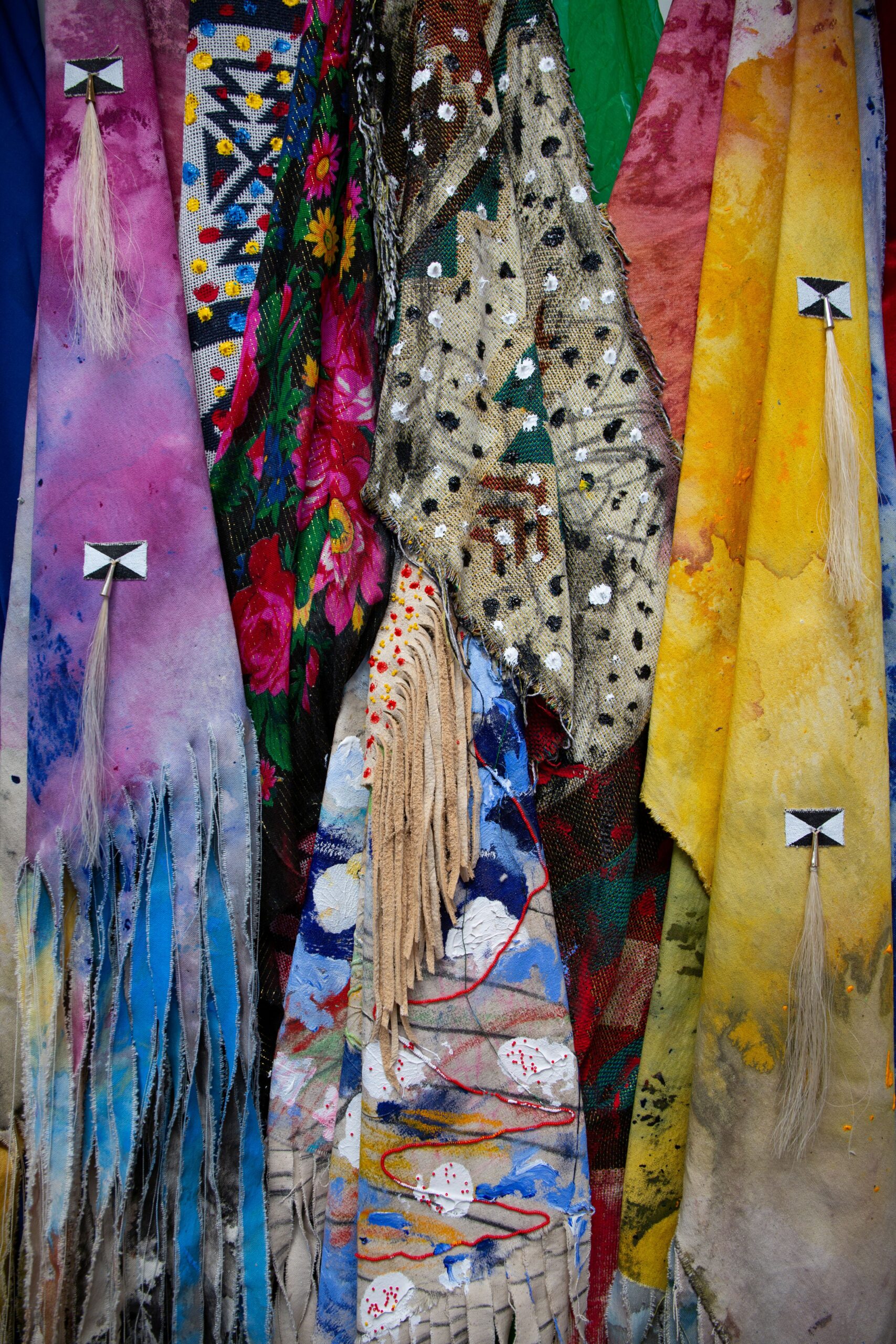 Detail of large unstretched canvases layered on top of each other. Colors are purple, blue, yellow and floral patterns